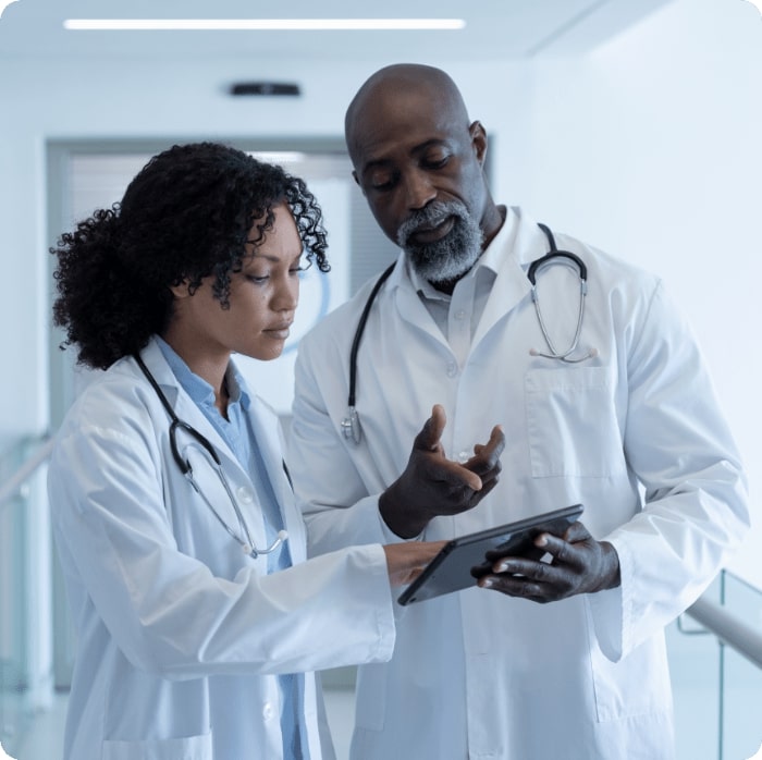 Diverse male and female doctor talking seriously and looking at digital tablet in hospital corridor. medicine, health and healthcare services.