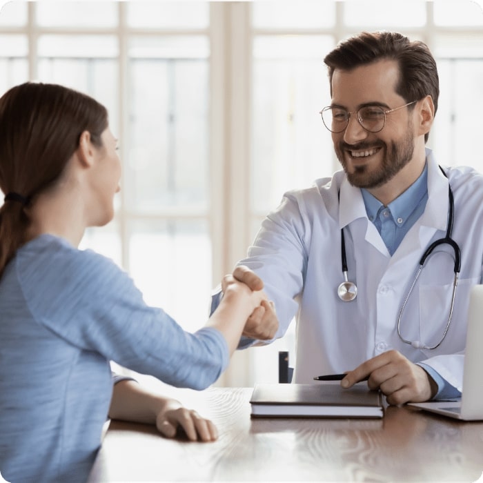 Smiling young Caucasian male doctor shake hand greeting get acquainted with female patient in hospital, happy man physician handshake woman client make agreement sign health insurance in clinic