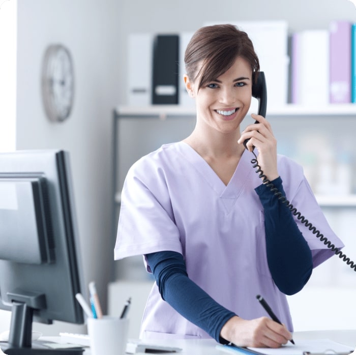 Young practitioner doctor working at the clinic reception desk, she is answering phone calls and scheduling appointments